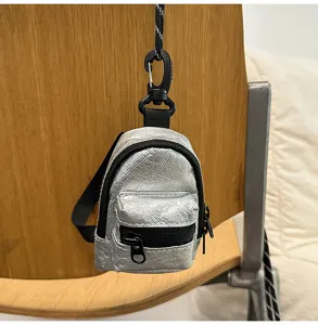 Vista detallada de la mini mochila plateada para auriculares, monedero con cremallera negra.