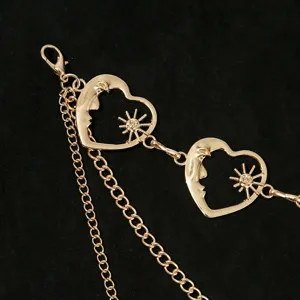 Gros plan détaillé de la chaîne de corps dorée avec pendentifs cœur soleil et lune et maillons.