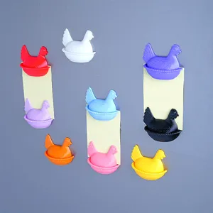 Detailed close-up of colorful 3d chicken fridge magnets holding sticky notes on metal surface.