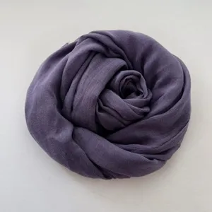 Primo piano dettagliato di una sciarpa in cotone e lino viola scuro arrotolata su sfondo bianco.