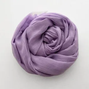 Dettaglio di sciarpa in cotone e lino viola arrotolata, consistenza morbida, elegante.