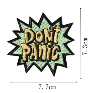 Detalle de parche bordado que muestra diseño de texto estilo cómic Don't Panic y medidas.