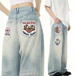 Jeans in denim ricamati in stile bohemien con testi motivazionali e toppe floreali.