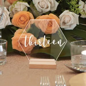 Detalle de letrero de número de mesa hexagonal acrílico con base de madera y fondo floral.