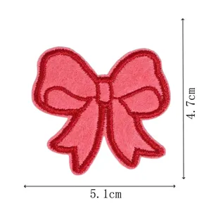 Close-up detail of pink embroidered bow patch with red border for clothing decoration and repair.