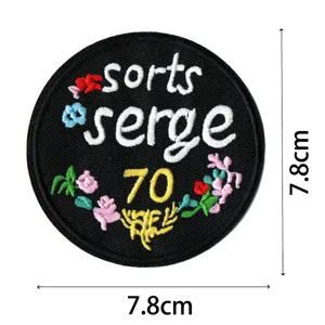 Round embroidered patch black cloth sticker with floral details and letters close up view