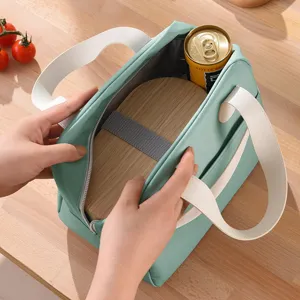 Geïsoleerde lunchtas van mintgroene stof met witte handvatten, open op houten tafel.