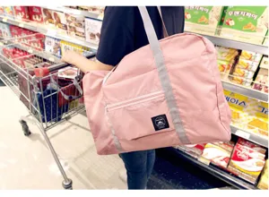 Vista detallada de la bolsa de viaje plegable de nylon rosa con correa y bolsillo delantero.