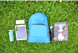 Vue de détail d'un sac à dos pliable bleu sur l'herbe avec divers accessoires de voyage.