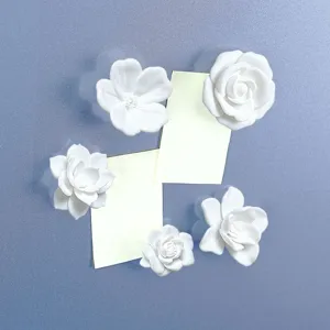 Detailed view of white 3D floral fridge magnets securely holding yellow sticky notes on surface.