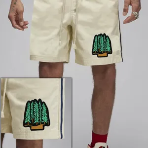 Men casual beige shorts with drawstring waist and detailed forest tree embroidery patch.