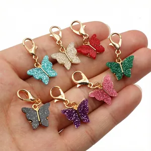 Close-up of colorful glitter acrylic butterfly charms with gold lobster clasps for DIY jewelry.