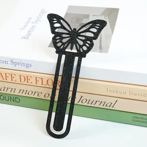Nahaufnahme eines glitzernden schwarzen Schmetterling-Lesezeichens auf gestapelten Büchern.
