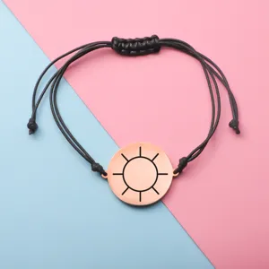 Closeup view of minimalist rose gold sun pendant on black braided cord bracelet detail.