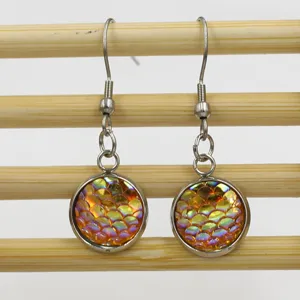 Close-up detail of stainless steel and resin round fish scale drop earrings on wooden rack.