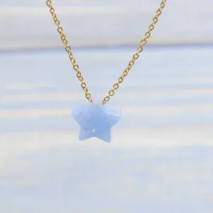 Close-up detail shot of a dainty gold chain necklace featuring a light blue resin star pendant.