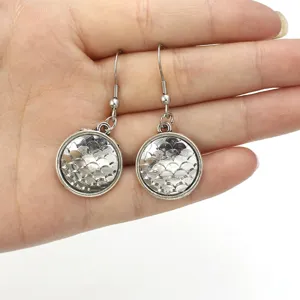 Detailed shot of silver round mermaid fish scale dangle earrings held in hand for women.