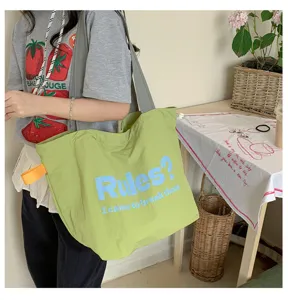 Casual light green canvas tote bag detail, featuring bold blue letter print and orange handle.