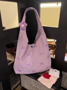 Detailed view of a purple embroidered tote bag with bow details and cute knit flower charm.