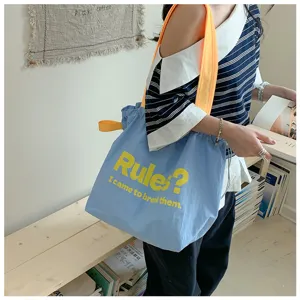 Blue canvas shoulder tote bag detailed view with yellow graphic slogan print in casual lifestyle.