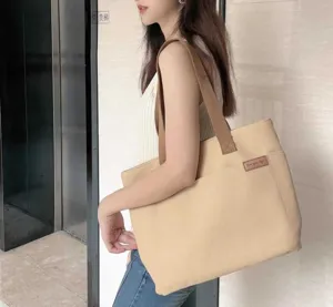 Detail shot of a beige canvas tote bag with brown straps, showing side wear and front pocket.