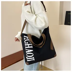 Vue détaillée du grand sac fourre-tout en toile noire avec lanières marron et lettres.