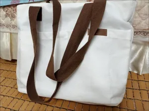 White canvas tote bag with brown straps, casual large capacity shoulder bag for daily commuting use.