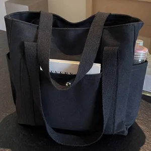 Detail view of the black canvas tote bag showing sturdy double handles and front pocket storage.