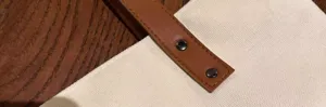 Close-up detail of canvas tote bag brown leather handle with metal rivet reinforcement.