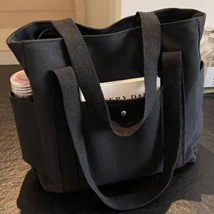 Detail view of black canvas tote bag with multiple side and front pockets for daily commute.