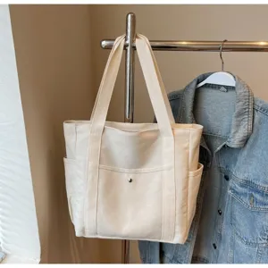 Casual beige canvas tote bag with shoulder straps and front pocket for daily commute and study.