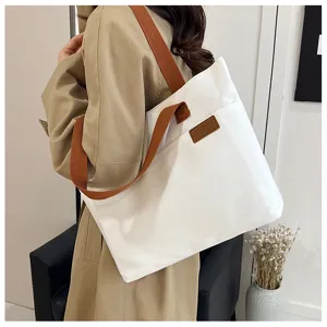 Casual white canvas tote bag with brown straps and front pocket for women daily commuting.