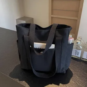 Black canvas tote bag detail view showing spacious front pocket structure and sturdy fabric.