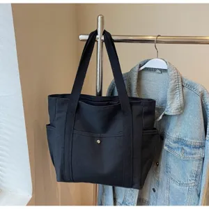 Detail view of black canvas tote bag hanging on rack with denim jacket, large daily commuter bag.