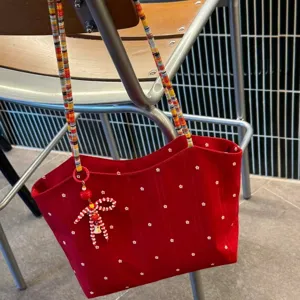 Red floral canvas tote bag detail view, showing colorful beaded strap and cute bow charm.