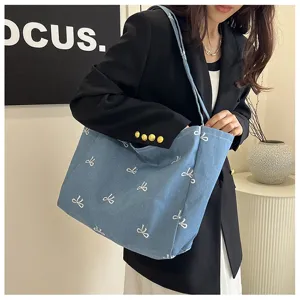 Detailed view of a blue denim tote bag with cute white bow patterns worn by model.