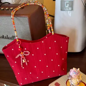 Red floral canvas tote bag detail view, featuring colorful woven shoulder strap and cute bow charm.