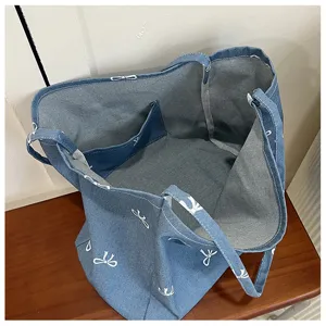 Blue denim tote bag interior detail view with white bow prints and inner pocket design.