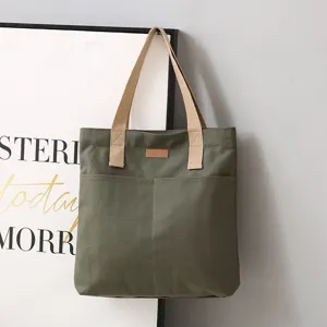 Canvas tote bag detail view showing dark green fabric, sturdy handles and dual front pockets.