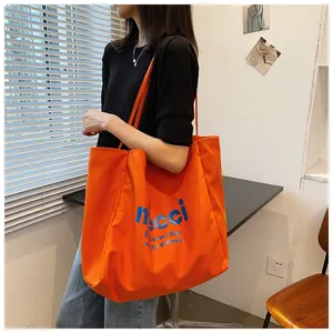 Detail view of a large capacity orange canvas tote bag with stylish blue letter print.