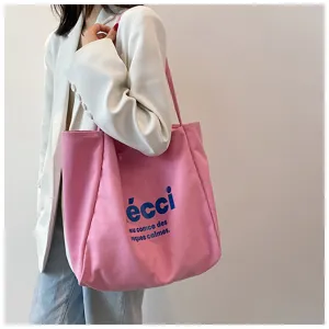 Detail shot of a pink canvas tote bag featuring blue printed text, ideal for daily casual use.