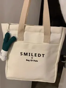 Canvas tote bag detail showcasing beige handles and a cute green plush toy pendant.