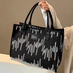 Canvas tote bag detail view showing black fabric texture and stylish wave embroidery pattern.