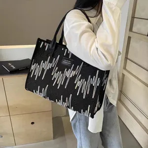 Detail shot of black canvas tote bag featuring unique white wave embroidery and dual handles.