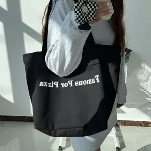 Detailed view of a black canvas tote bag with white letter print, casual style daily use.