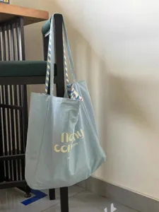 Detail view of the light blue canvas tote bag featuring stylish striped shoulder straps.