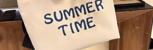 Detail view of the beige canvas tote bag featuring stylish blue embroidered lettering.