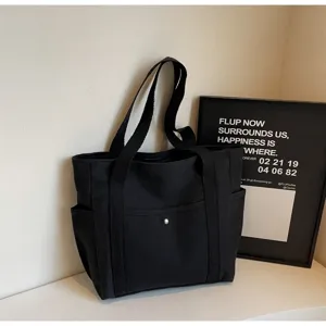 Detailed view of the black canvas tote bag showing front pocket and sturdy shoulder straps.