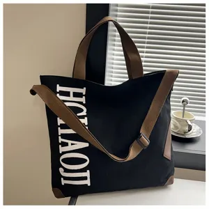 Vue détaillée d'un grand sac cabas en toile noire avec des lanières marron et du texte.