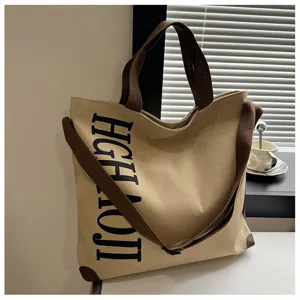 Grand sac cabas en toile avec bandoulières marron et détail d'impression de lettres verticales.